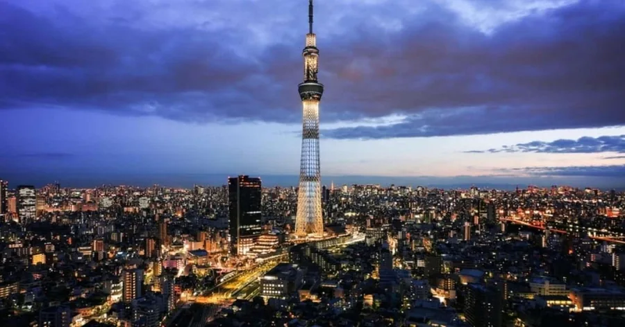 夕暮れどき、低い街並みの上にそびえるライトアップされた東京スカイツリー