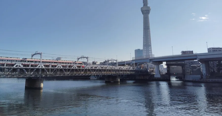 晴れた日、隅田川にかかる鉄橋の向こうにそびえる東京スカイツリー